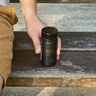 Hand holding a jar of Concentrated Organic Reishi Mushroom Powder with a natural backdrop